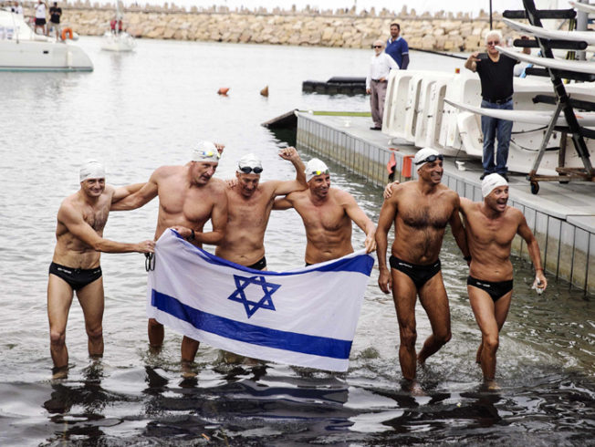 Six Israeli swimmers hold the Israeli flag during a media presentation, a day after their attempt to claim the Guinness world record for open-water relay distance swimming, in the Herzliya Marina, near Tel Aviv